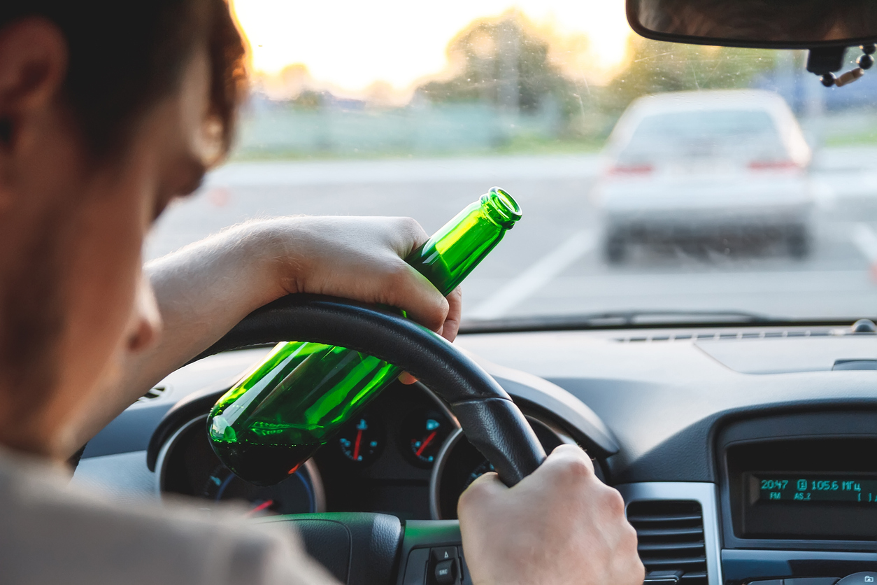 Drunk young man driving a car with a bottle of beer which represents the dui personal injury cases Howell and Thornhill take on.